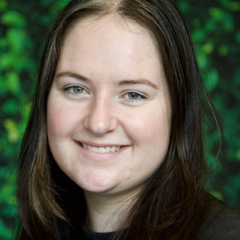 A photo of Eva Muller wearing a black shirt with a green background.
