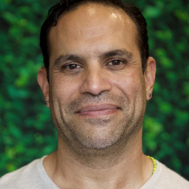 A photo of Jesse Ontiveros wearing an off-white shirt with a green background.